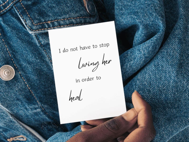 Card reading I do not have to stop loving her in order to heal held against a denim background