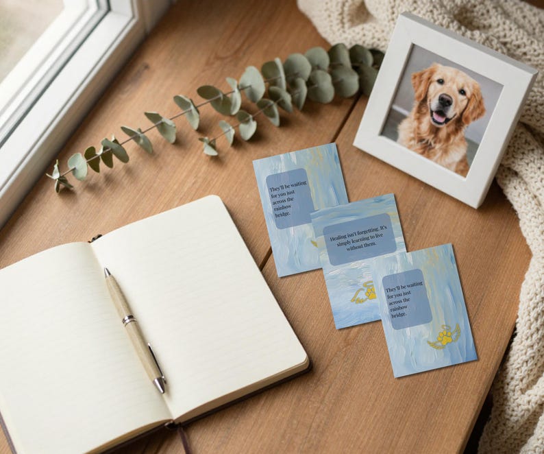 Cards arranged on a wood table with an open grief journal eucalyptus and framed Golden Retriever photo